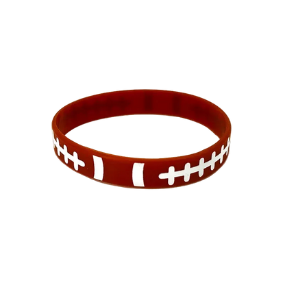 A red silicone wristband designed to look like a football, featuring white laces and stripes, photographed on a clean white background.