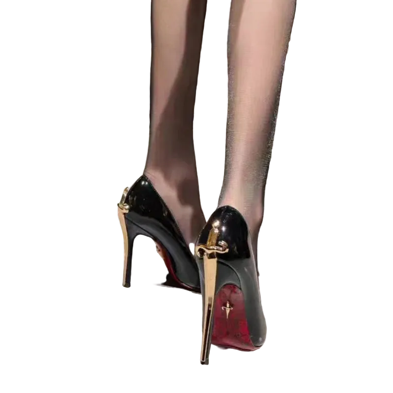 A close-up of a person wearing glossy black patent stiletto pumps with gold-tone hardware and red soles, standing on a light gray tiled floor.