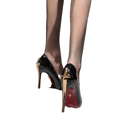 A close-up of a person wearing glossy black patent stiletto pumps with gold-tone hardware and red soles, standing on a light gray tiled floor.