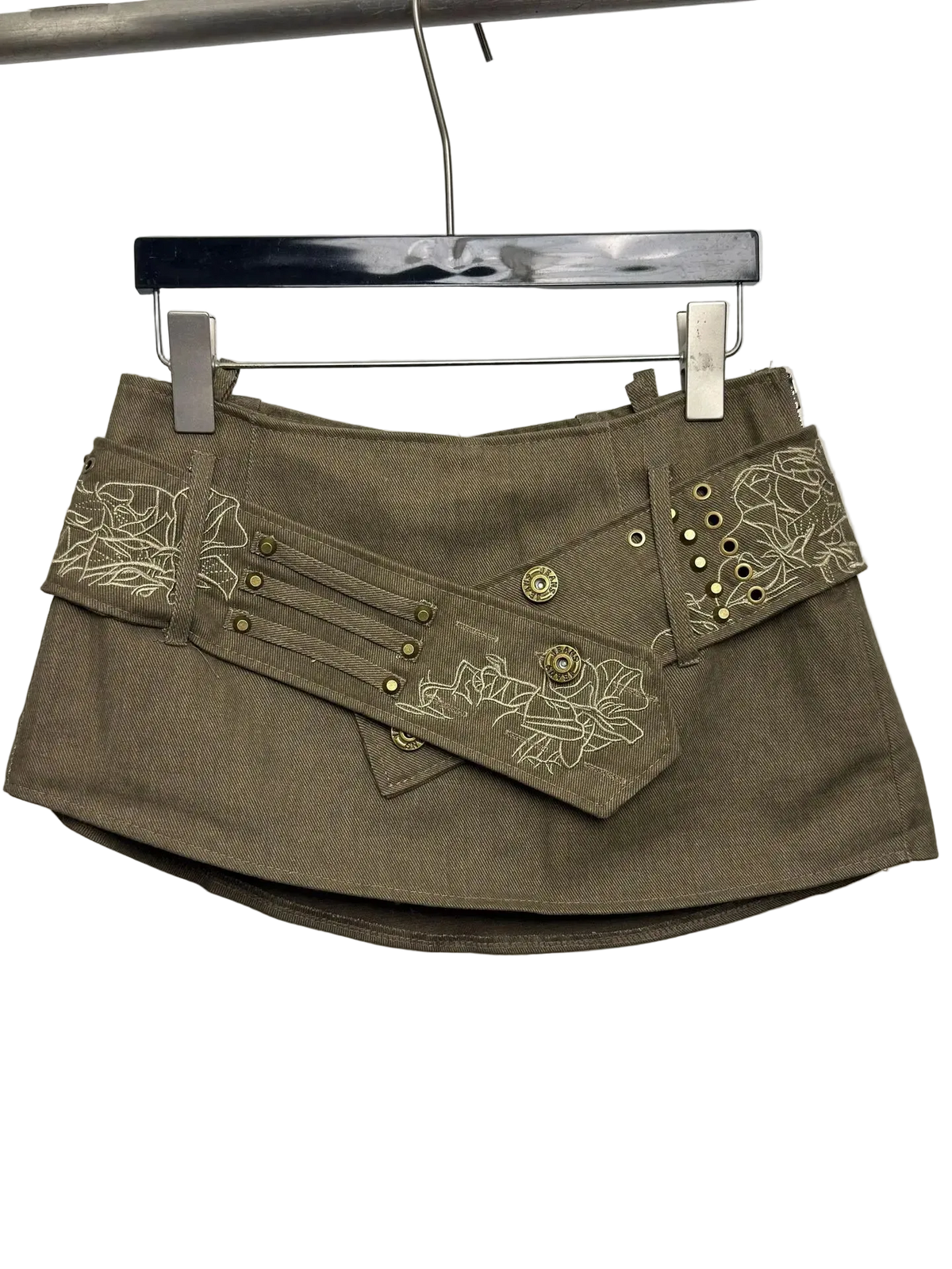 An olive brown mini skirt with decorative floral embroidery and brass grommets, hanging on a black hanger against a plain white background.