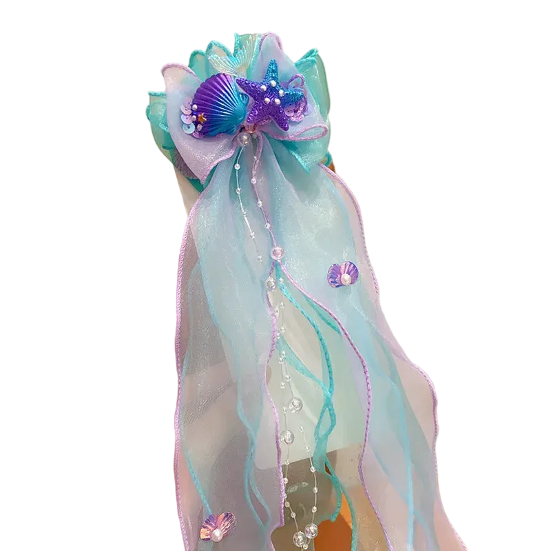 Decorative hair bow with ribbons and embellishments held by a hand against a neutral background