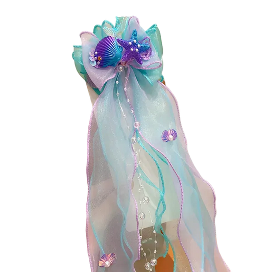 Decorative hair bow with ribbons and embellishments held by a hand against a neutral background