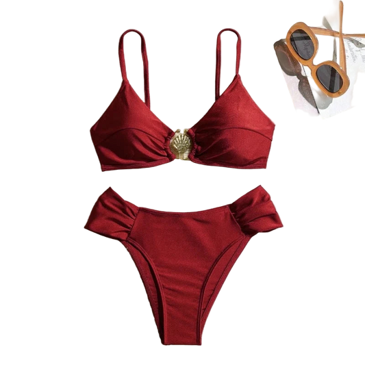Red bikini set on a textured surface with sunglasses and a magazine in the background.