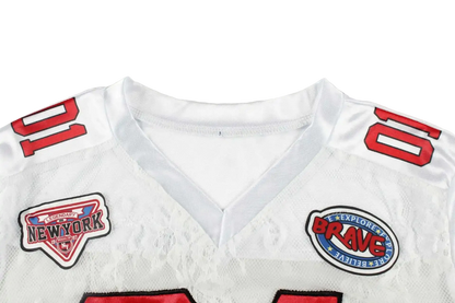 Close-up of a white sports jersey with red shoulder numbers and two embroidered patches on the chest, photographed against a light gray background.