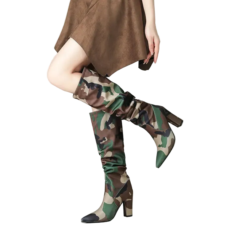 A model's legs wearing a pair of knee-high camouflage boots with a pointed toe and block heel, paired with a brown dress against a clean studio background.