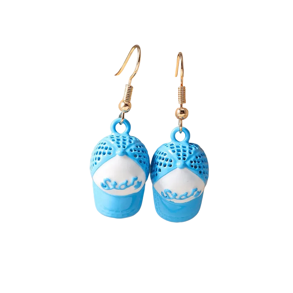 A pair of dangling earrings shaped like blue and white baseball caps, displayed on a beige jewelry stand against a soft neutral background.