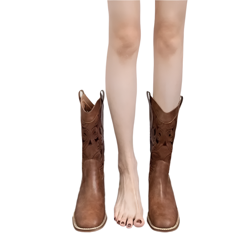 Brown cowboy boots worn by a person on a wooden floor with a white background
