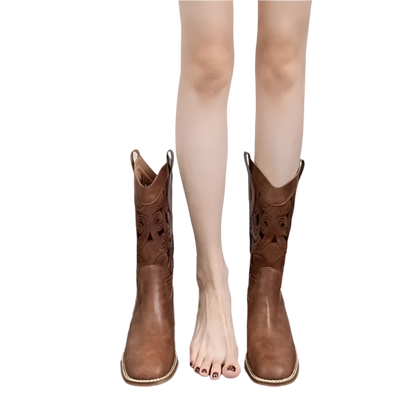 Brown cowboy boots worn by a person on a wooden floor with a white background