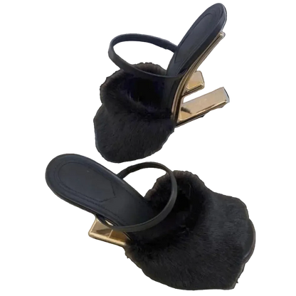 Black sandals with fur details on a gold platform on a wooden surface.