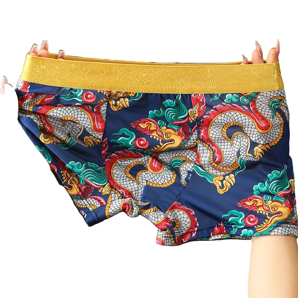 Colorful dragon-patterned shorts with a yellow waistband held by hands against a gray background.
