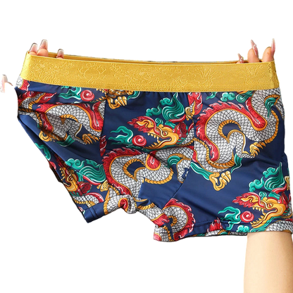 Colorful dragon-patterned shorts with a yellow waistband held by hands against a gray background.