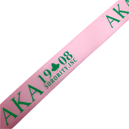 Pink sash with green text 'AKA 1908 Sorority, Inc.' on a light blue background