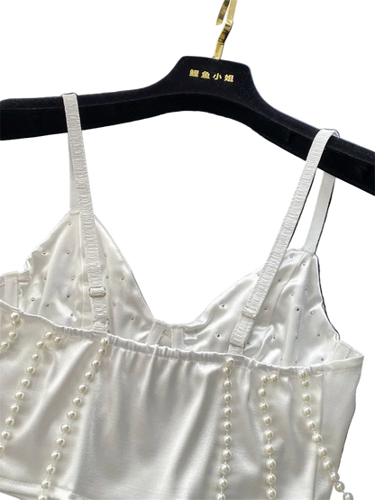 White satin top with pearl embellishments on a black hanger against a gray background.