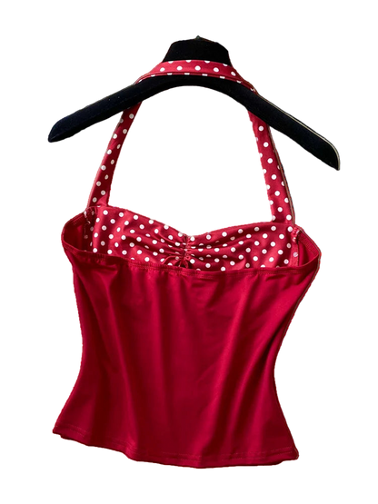 Red polka dot top on a hanger with a straw hat and pearl necklace on a textured surface.