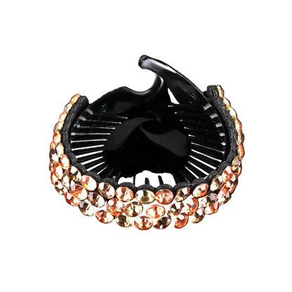 A black hair claw clip embellished with rows of rose gold rhinestones, shown on a reflective black background.