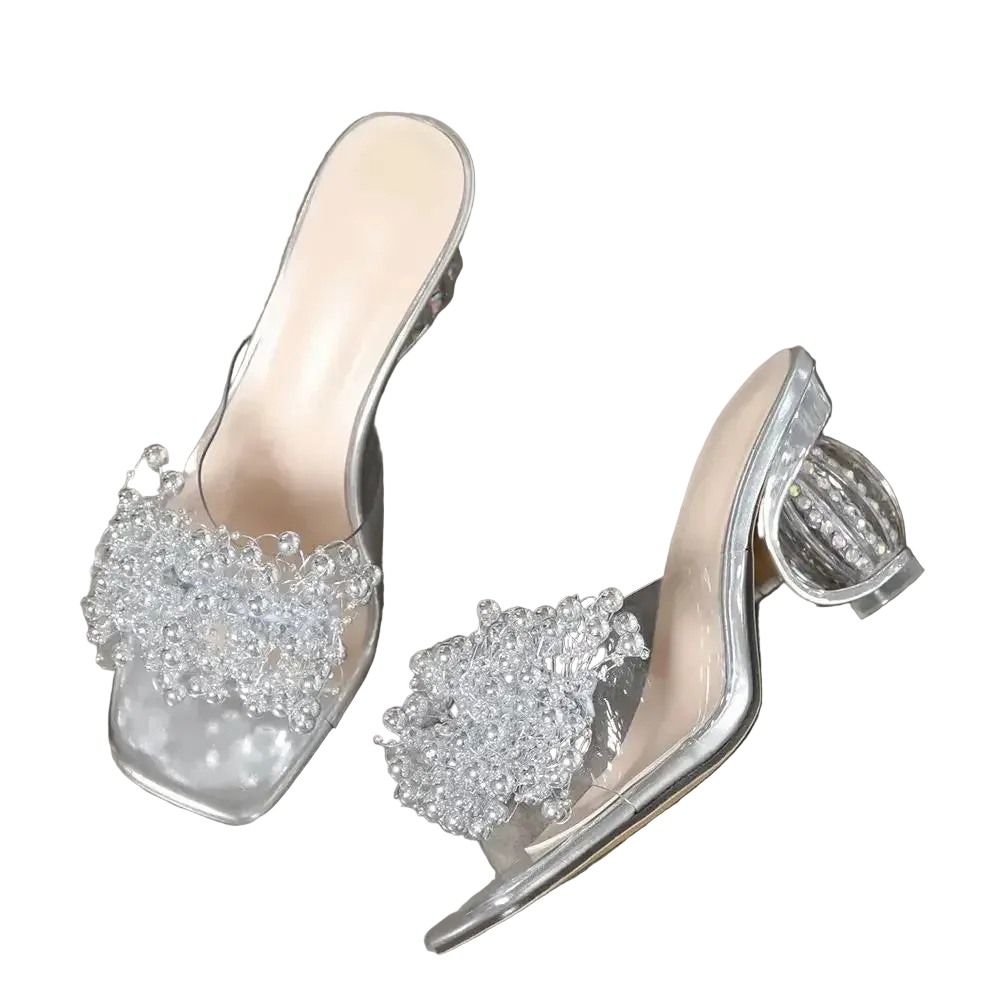 Clear high-heeled shoes with embellishments on a gray surface, 