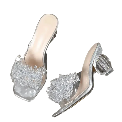 Clear high-heeled shoes with embellishments on a gray surface, 