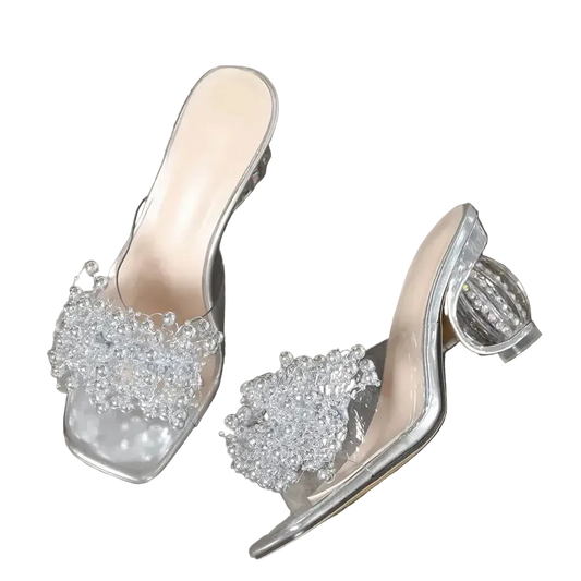 Clear high-heeled shoes with embellishments on a gray surface, 