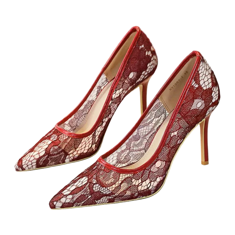 A pair of pointed-toe high heels with a red and beige floral lace pattern, shown on a white surface with a shoe box in the background