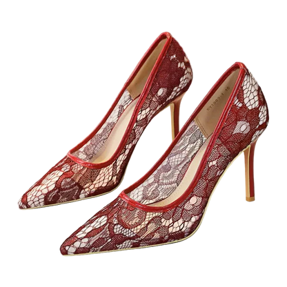 A pair of pointed-toe high heels with a red and beige floral lace pattern, shown on a white surface with a shoe box in the background