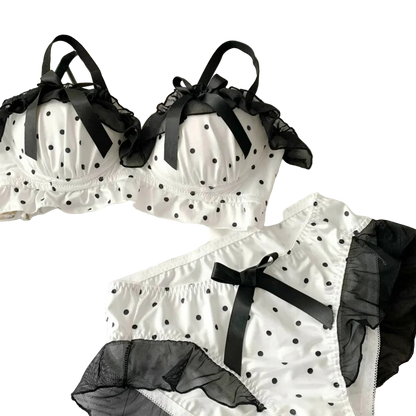 White polka dot lingerie set with black ribbons on a white surface.