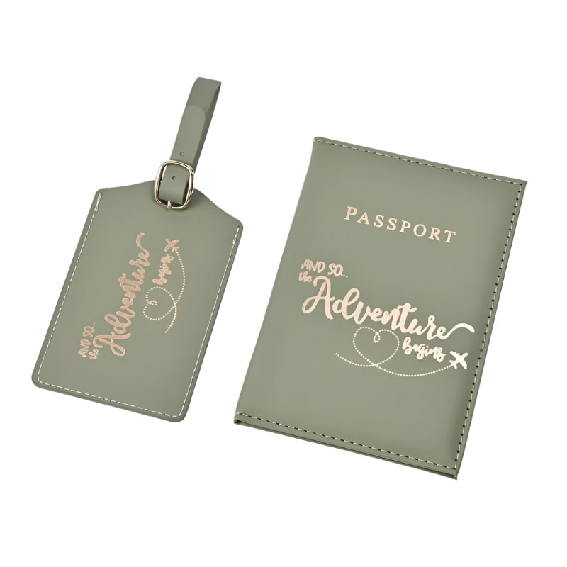 A passport holder and luggage tag set with the phrase "And so the adventure begins" in elegant script. The design is sleek and stylish, perfect for travel.