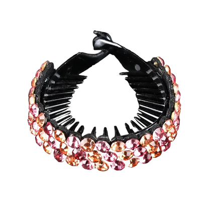 A black hair claw clip embellished with rows of faceted pink and orange rhinestones, displayed on a reflective black surface.