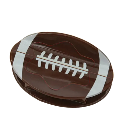 A football-shaped chocolate bar or candy bar in glossy dark brown with white laces and white side stripes, photographed on a plain light beige background.