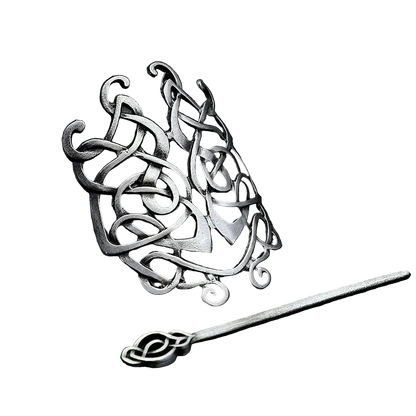 Silver hairpin with intricate designs on a dark textured surface