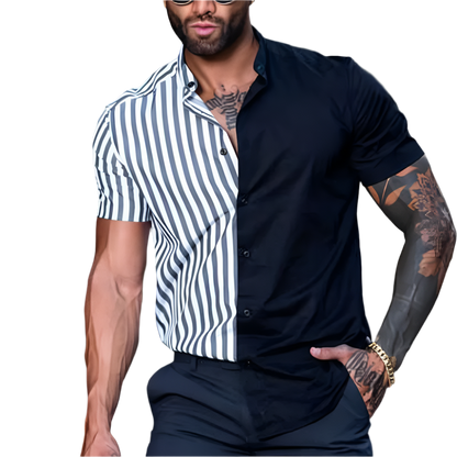 Man wearing a black and white striped shirt over a black shirt with tattoos on arms, sitting against a blurred background.