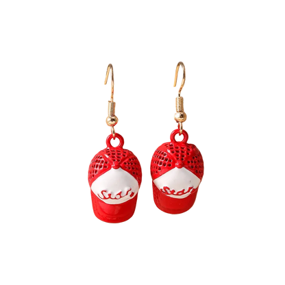 A pair of dangling earrings shaped like red baseball caps with white panels and the word 'State' in script, hanging from gold-tone hooks on a beige display stand.
