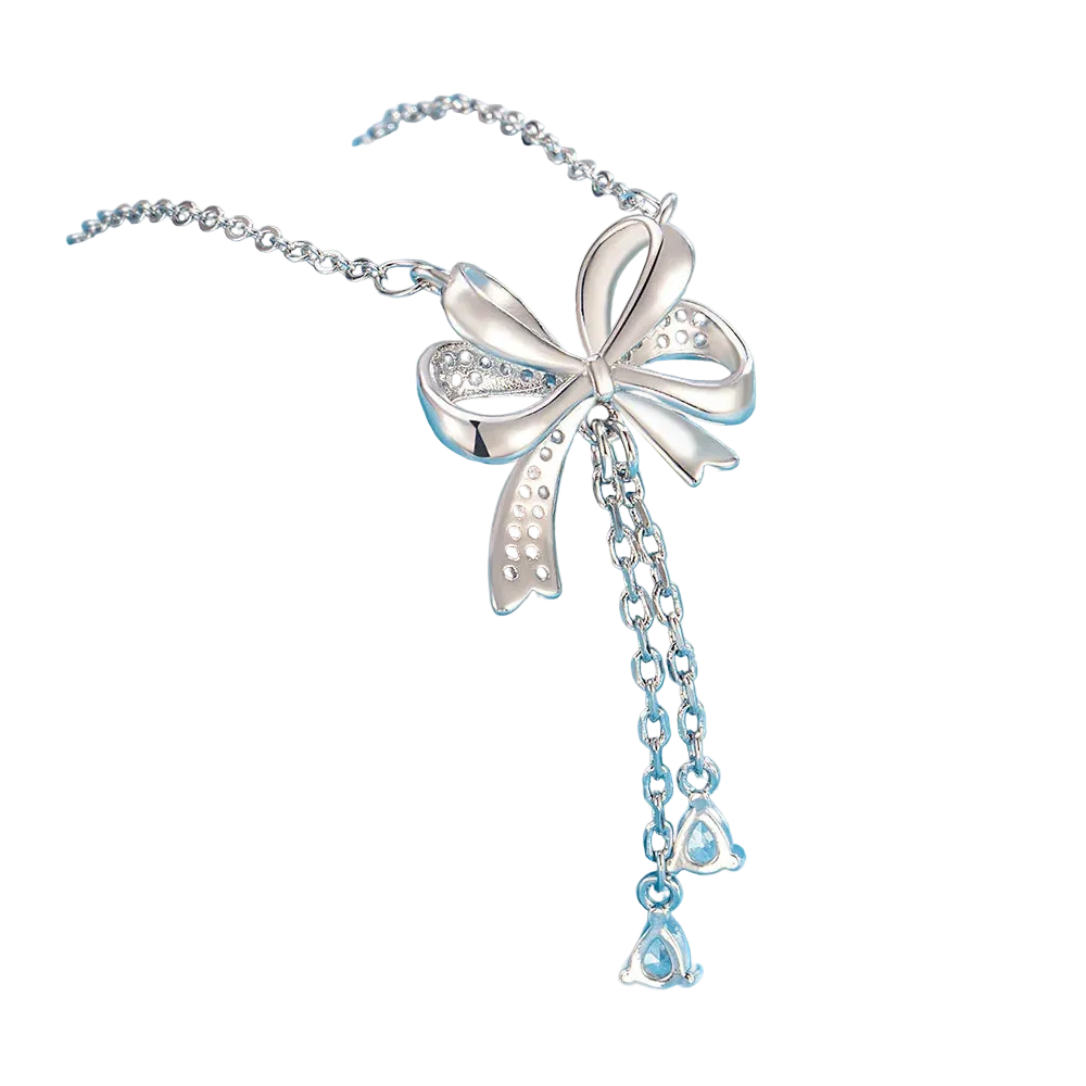 A silver-toned bow pendant necklace with dangling chain and clear teardrop-shaped stones, displayed on a light blue cylindrical stand against a soft blue background.