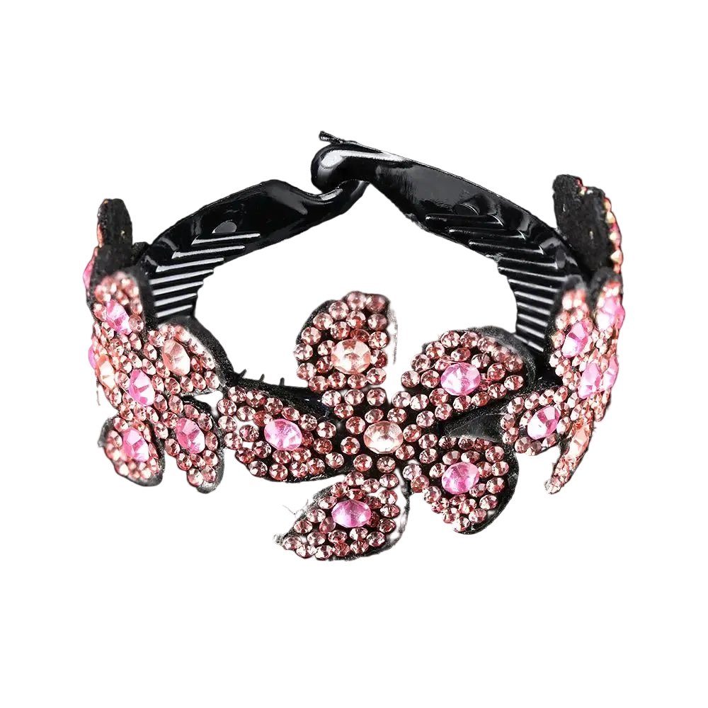 A black hair claw clip decorated with pink rhinestones in a floral pattern, shown on a reflective black background.