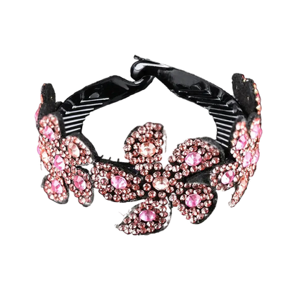 A black hair claw clip decorated with pink rhinestones in a floral pattern, shown on a reflective black background.