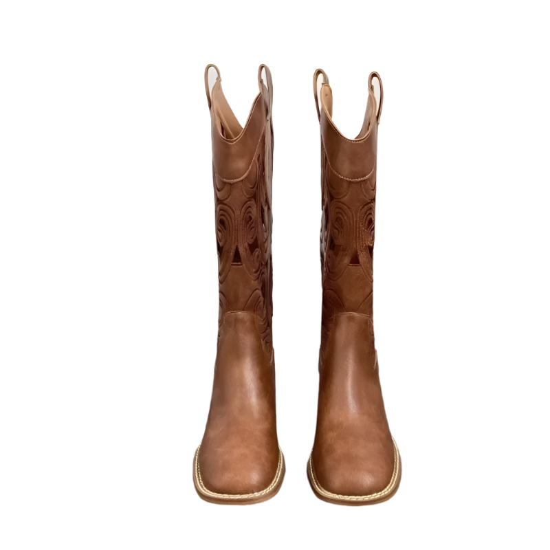 Pair of brown cowboy boots on a wooden floor with a white wall in the background.