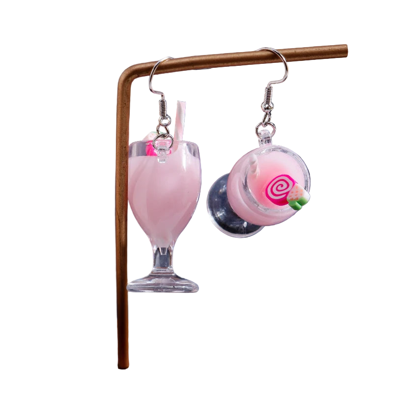Earrings shaped like pink milkshakes with a straw on a stand against a dark background
