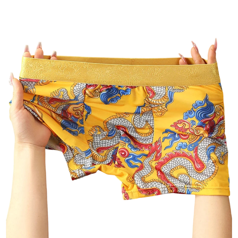 Yellow boxer briefs with dragon pattern held by a person on a white background