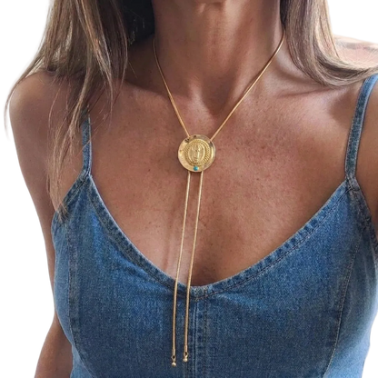 A gold-toned lariat necklace with a circular pendant featuring a religious figure, worn by a model in a blue denim camisole top.