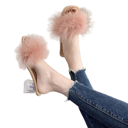 Pink fuzzy sandals worn with blue jeans on a reflective surface.