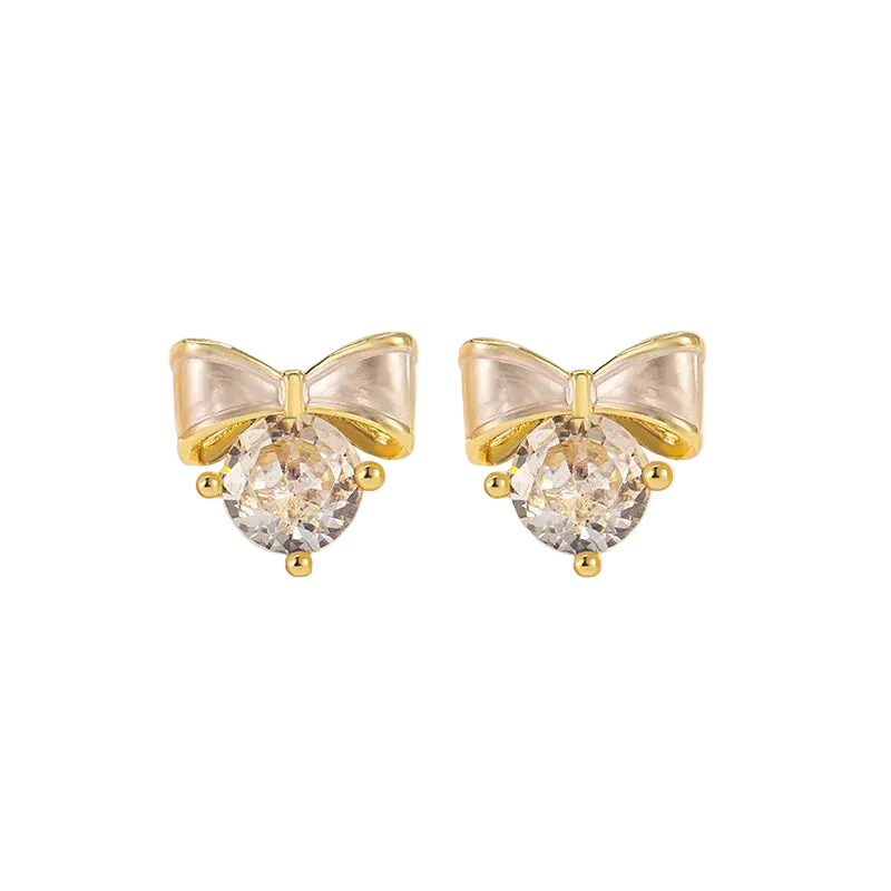 A pair of gold bow stud earrings with clear faceted round crystals, displayed on a white decorative surface.