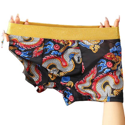 Colorful dragon-patterned boxer briefs with a yellow waistband held by hands against a gray background.