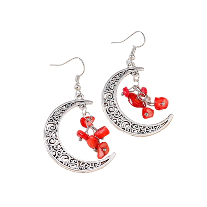 Silver earrings with red beads on a textured beige surface