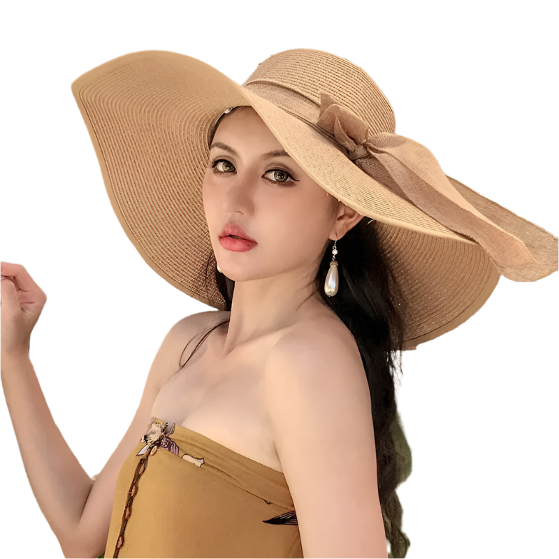 Woman wearing a large beige sun hat in an outdoor setting with plants and a building in the background.