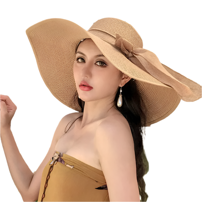 Woman wearing a large beige sun hat in an outdoor setting with plants and a building in the background.