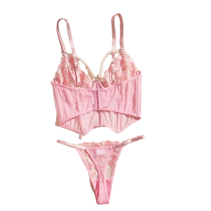 Pink lingerie set on a white surface with a beige jacket and decorative items.