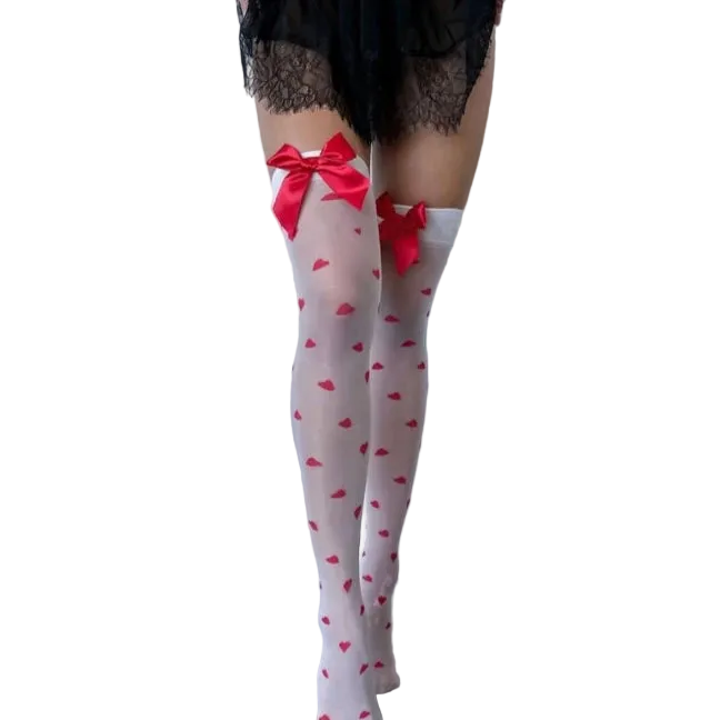 White thigh-high stockings with a red heart pattern and red bow accents at the top, worn by a model in a minimalist studio setting.