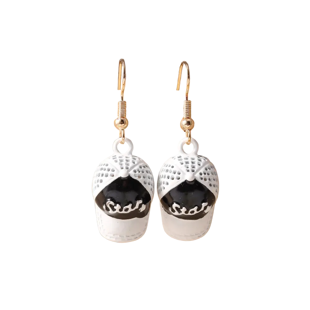 A pair of dangling earrings shaped like baseball caps in white and black, hanging from gold fishhook wires on a beige display stand.