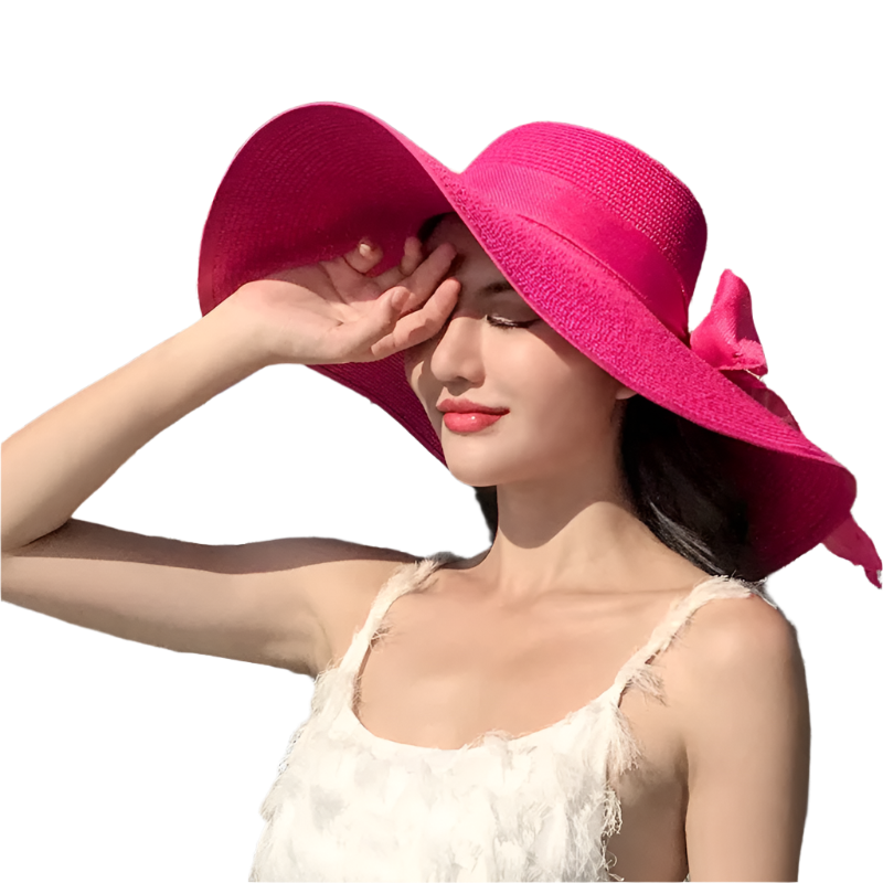 Woman wearing a bright pink hat with a large bow, standing outdoors with buildings and trees in the background.