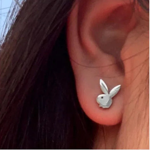 A close-up of a person's ear wearing a small silver bunny stud earring.