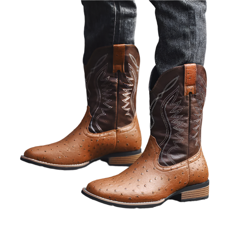 Brown cowboy boots with detailed stitching worn by a person on a gray pavement.